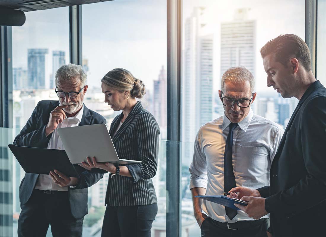 Directors and Officers Liability Insurance - Group of Business Directors and Colleagues Having a Work Discussion over Laptops While Standing in Front of Pane Glass Windows Indoors