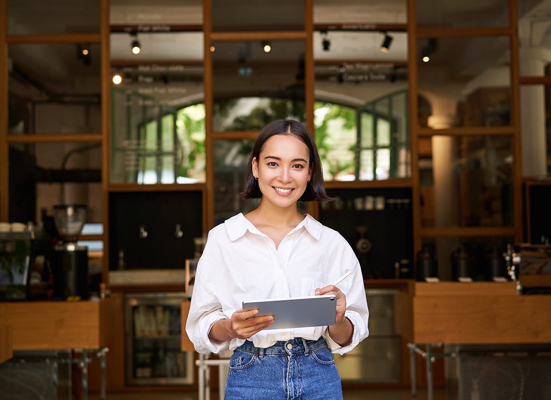 Business Insurance - Portrait of a Cheerful Young Woman Standing in a Commercial Property While Holding a Tablet in her Hands