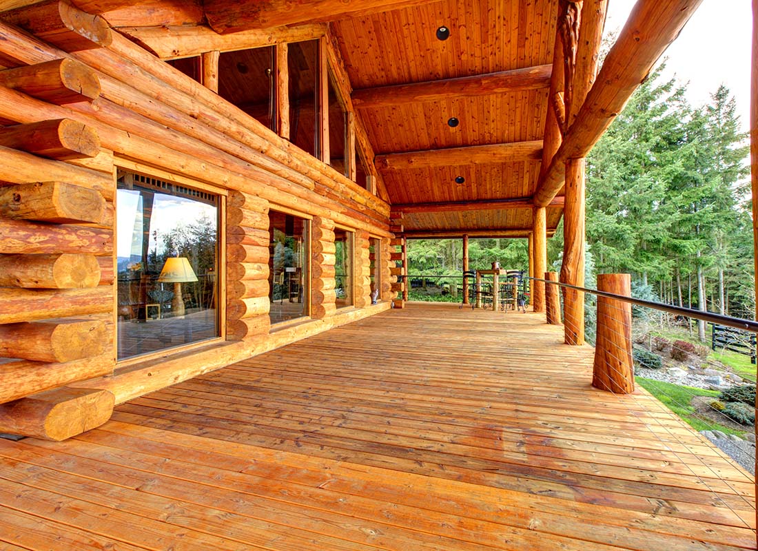 Insurance by Industry - View of a Custom Log Cabin Home with a Large Porch in a Scenic Area with Green Trees on a Sunny Day