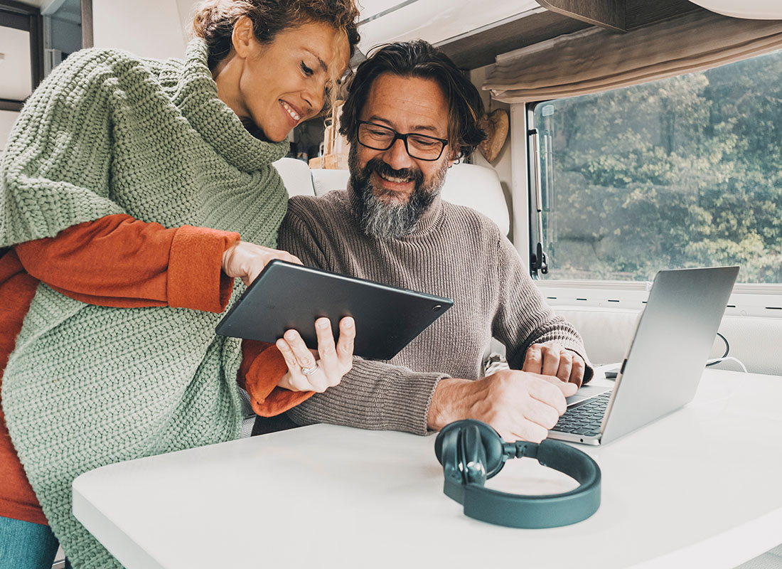 Pay Bill - Cheerful Middle Aged Couple Inside a Recreational Vehicle in the Forest Looking at a Tablet Together While on Vacation